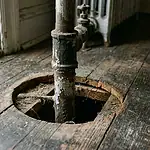 Radiator steam pipe penetration through apartment floorboards showing gap where mice travel between units